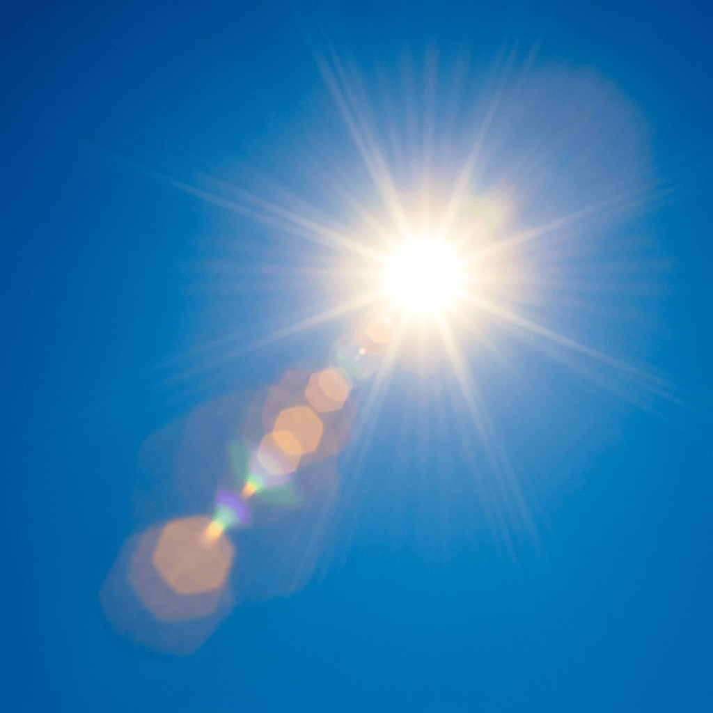 Bright sun with radiating light rays and hexagonal lens flare against blue sky